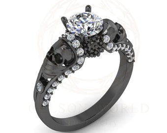 May include: Black engagement ring with a large round diamond and two skull accents. The ring is set in black metal and features a row of small diamonds around the band.