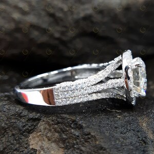 May include: A silver engagement ring featuring a large, round, clear centre stone surrounded by smaller stones. The band is decorated with multiple rows of smaller stones.
