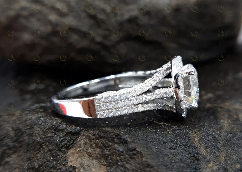 May include: A silver engagement ring featuring a large, round, clear centre stone surrounded by smaller stones. The band is decorated with multiple rows of smaller stones.