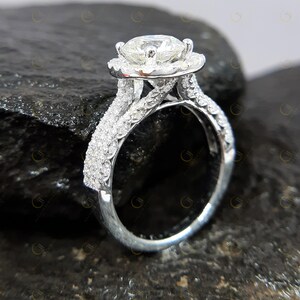 May include: A silver engagement ring featuring a large round centre stone surrounded by a halo of smaller stones. The band is a double band with a twisted design and is set with smaller stones.