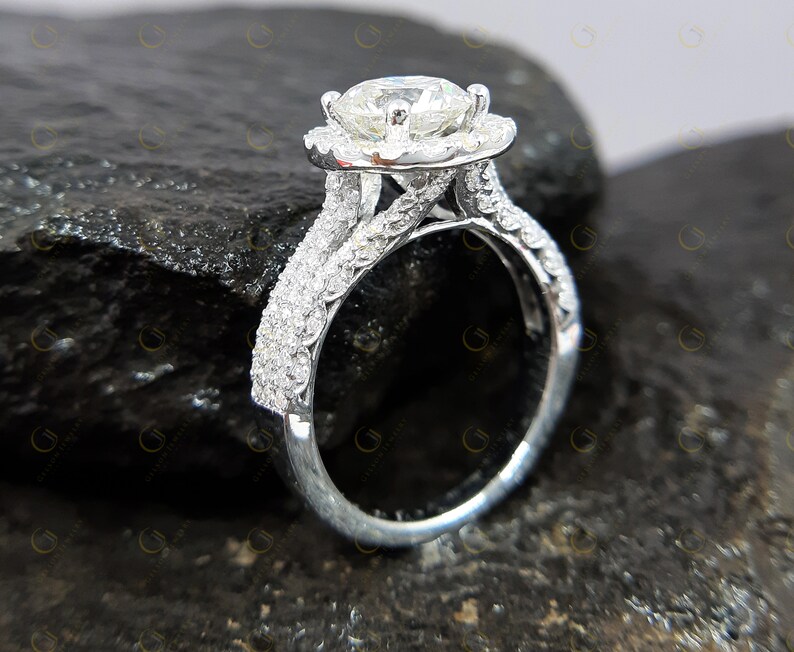 May include: A silver engagement ring featuring a large round centre stone surrounded by a halo of smaller stones. The band is a double band with a twisted design and is set with smaller stones.