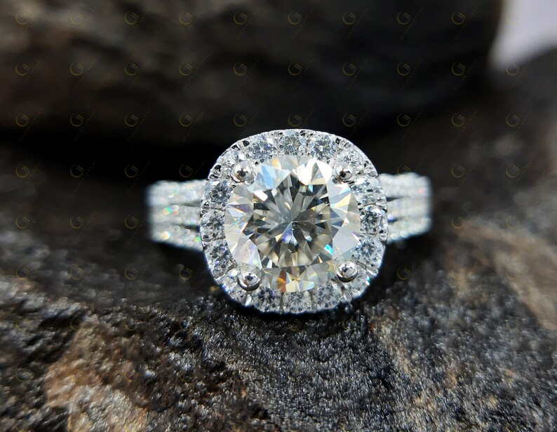May include: A silver engagement ring featuring a large, round, clear diamond centre stone encircled by a halo of smaller diamonds. The band has three rows of smaller diamonds.
