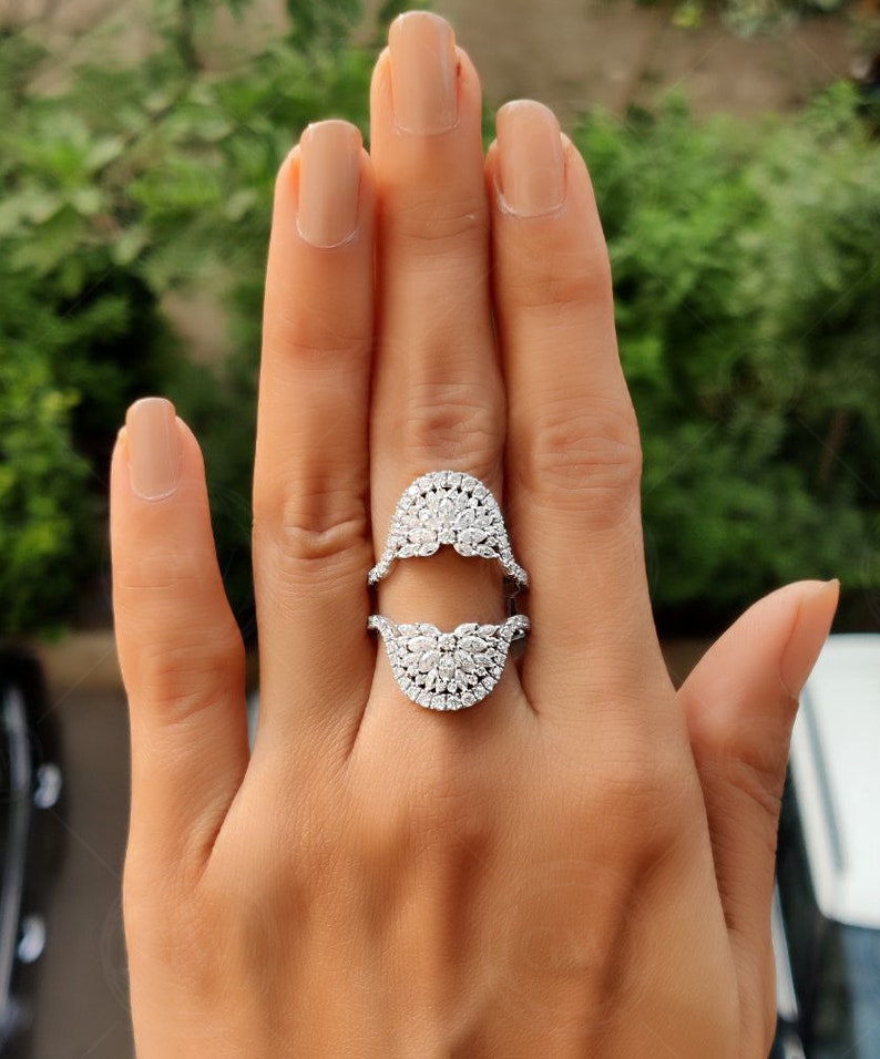 May include: A silver ring with a split design, featuring two half-circles of pave-set diamonds. The ring is worn on a person's finger.