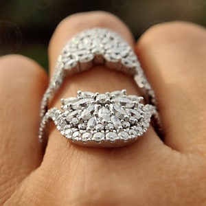 May include: A silver ring with a large, intricate design of sparkling white stones. The ring is worn on a finger and the design is centered on the top of the finger.