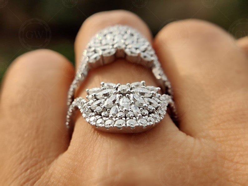 May include: A silver ring with a large, intricate design of sparkling white stones. The ring is worn on a finger and the design is centered on the top of the finger.