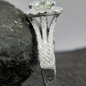 May include: A silver engagement ring featuring a large round centre stone encircled by a halo of smaller stones. The band is split into three prongs and is also set with smaller stones.