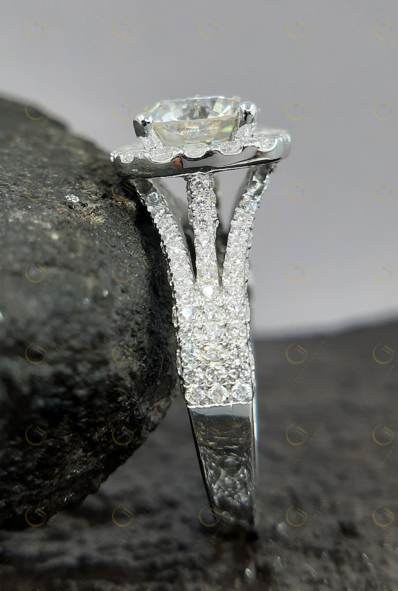 May include: A silver engagement ring featuring a large round centre stone encircled by a halo of smaller stones. The band is split into three prongs and is also set with smaller stones.