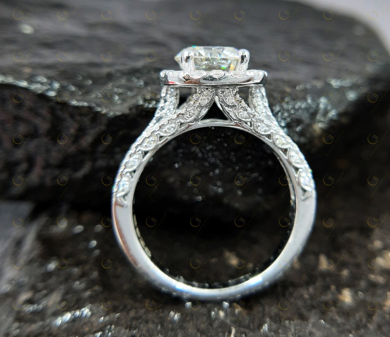 May include: A silver engagement ring featuring a large, round, clear centre stone surrounded by smaller stones. The band is also set with smaller stones and has a delicate, intricate design.