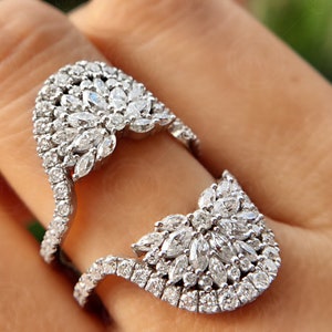 May include: A silver ring with a large, intricate design of pave-set diamonds. The ring is designed to be worn on two fingers.