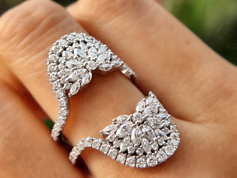 May include: A silver ring with a large, intricate design of pave-set diamonds. The ring is designed to be worn on two fingers.