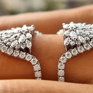 May include: A silver ring with a large, intricate design of pave-set diamonds. The ring is open in the back and has a curved shape.