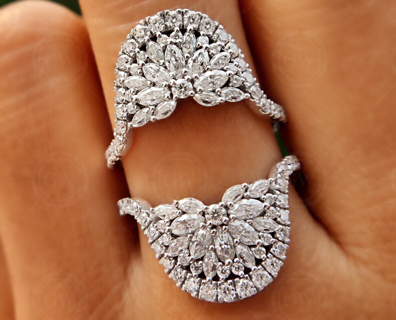 May include: Two silver rings with a design of small, clear diamonds set in a flower-like pattern. The rings are worn on a finger.