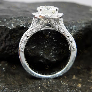 May include: A silver engagement ring featuring a large, round, centre diamond surrounded by a halo of smaller diamonds. The band is also set with smaller diamonds.