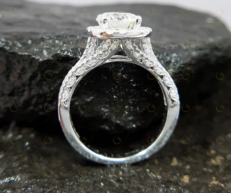 May include: A silver engagement ring featuring a large, round, centre diamond surrounded by a halo of smaller diamonds. The band is also set with smaller diamonds.