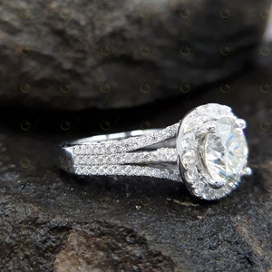 May include: A silver engagement ring featuring a large round centre stone surrounded by a halo of smaller stones. The band has three rows of smaller stones.