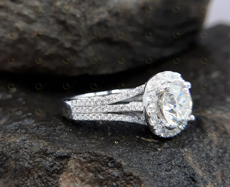May include: A silver engagement ring featuring a large round centre stone surrounded by a halo of smaller stones. The band has three rows of smaller stones.