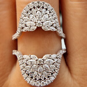 May include: A pair of silver rings with a unique design featuring a cluster of small, round diamonds set in a delicate, curved shape. The rings are stacked on top of each other, creating a layered look.