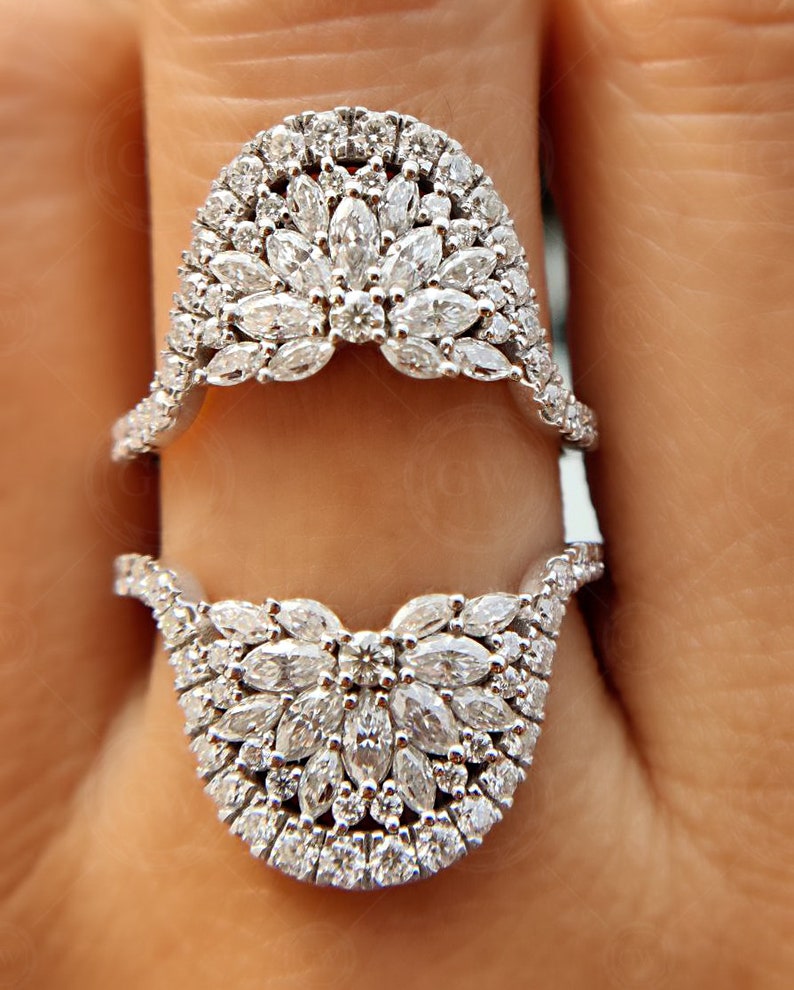May include: A pair of silver rings with a unique design featuring a cluster of small, round diamonds set in a delicate, curved shape. The rings are stacked on top of each other, creating a layered look.
