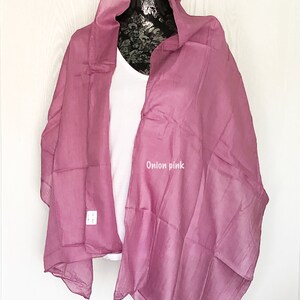 May include: A soft, sheer, onion pink scarf draped over a white shirt on a mannequin. The scarf is made of a lightweight fabric and has a delicate drape.