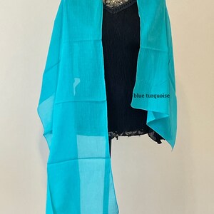 May include: A light blue sheer scarf draped over a mannequin. The scarf is made of a soft, flowing fabric and has a subtle sheen. The text "blue turquoise" is written on the scarf.