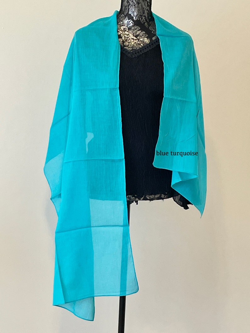 May include: A light blue sheer scarf draped over a mannequin. The scarf is made of a soft, flowing fabric and has a subtle sheen. The text "blue turquoise" is written on the scarf.