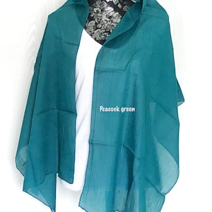 May include: A peacock green sheer scarf draped over a white shirt on a mannequin. The scarf is made of a lightweight fabric and has a soft, flowing drape.
