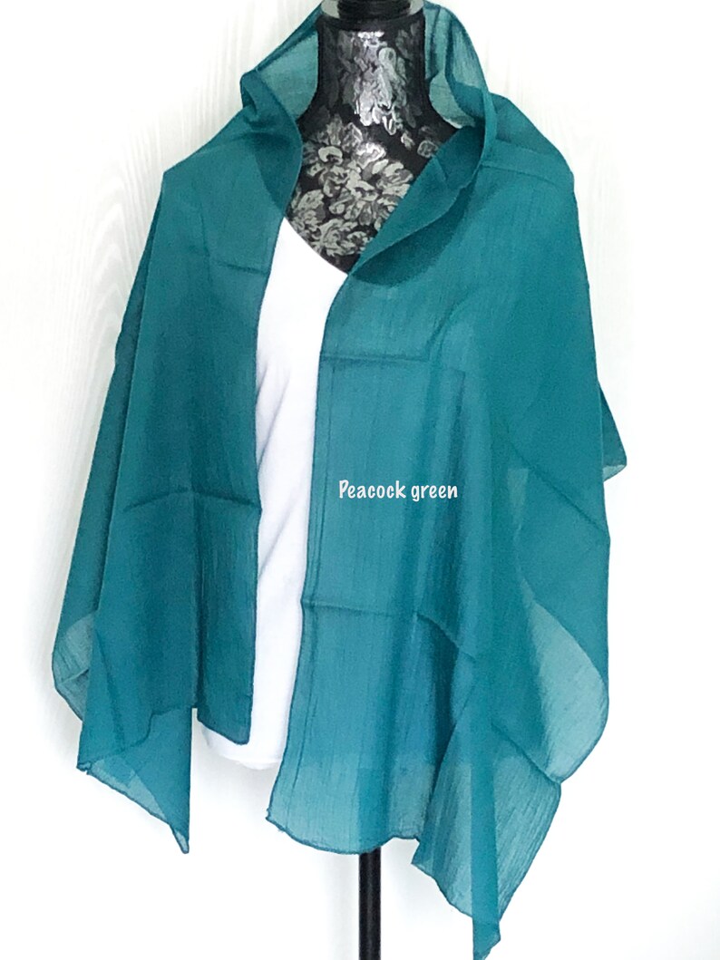 May include: A peacock green sheer scarf draped over a white shirt on a mannequin. The scarf is made of a lightweight fabric and has a soft, flowing drape.