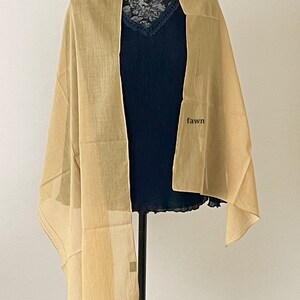 May include: A light brown sheer scarf draped over a mannequin. The scarf is made of a lightweight fabric and has a subtle sheen. The word "fawn" is written on the mannequin's chest.