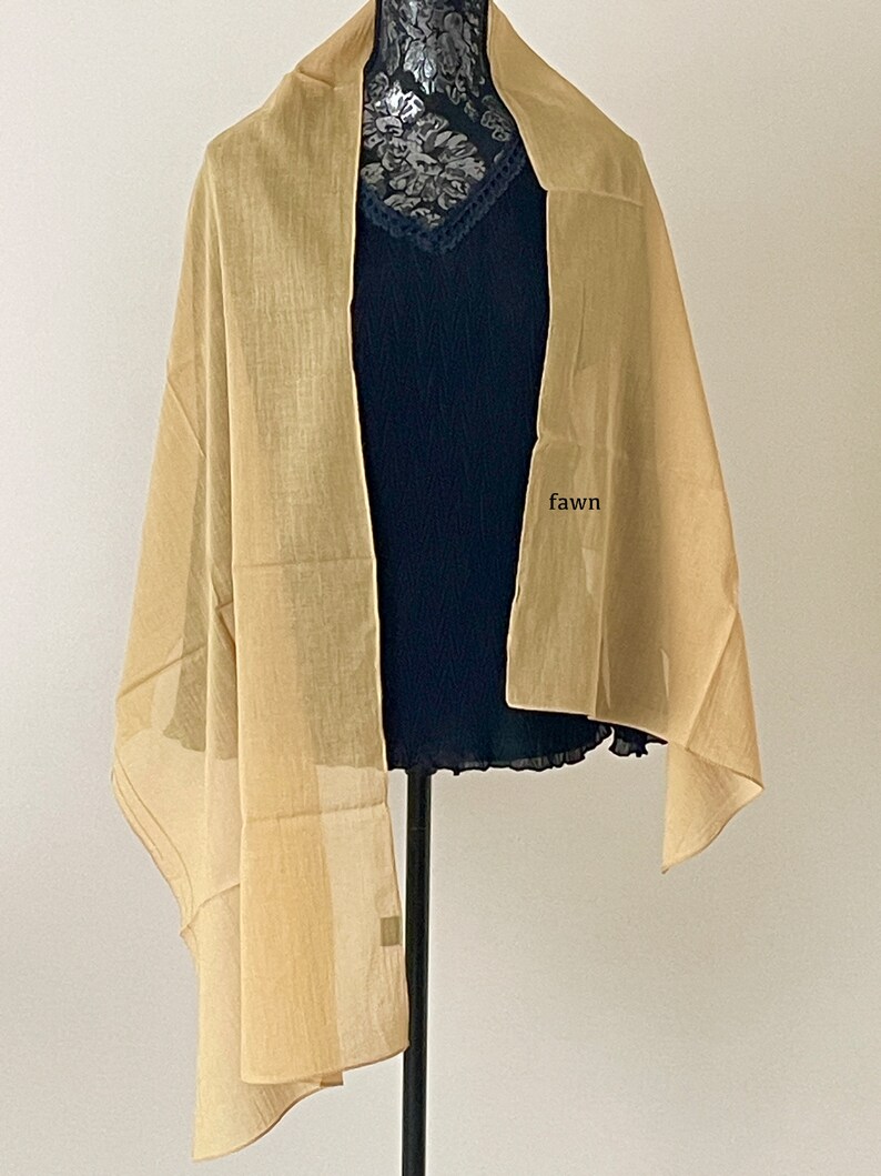 May include: A light brown sheer scarf draped over a mannequin. The scarf is made of a lightweight fabric and has a subtle sheen. The word "fawn" is written on the mannequin's chest.