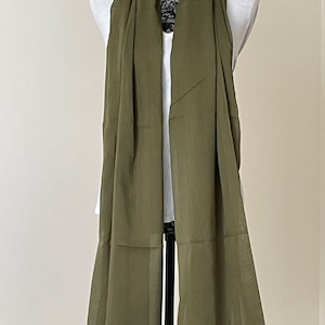 May include: A long, olive green scarf made of a lightweight fabric. The scarf is draped over a mannequin.