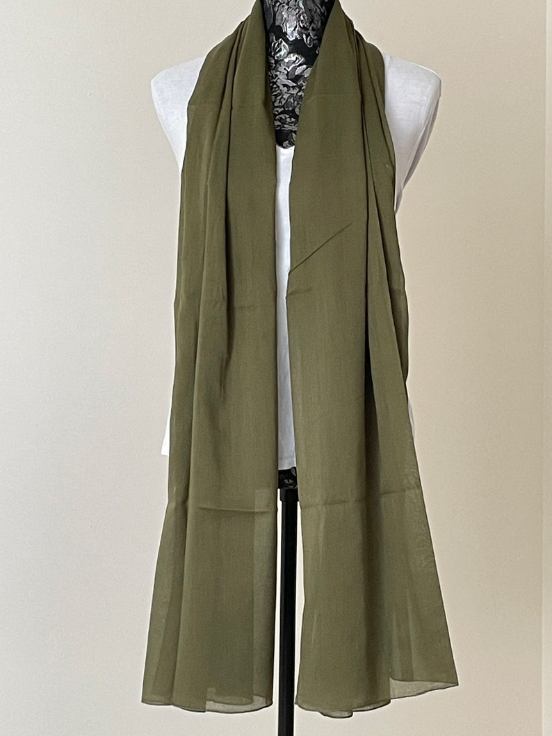 May include: A long, olive green scarf made of a lightweight fabric. The scarf is draped over a mannequin.