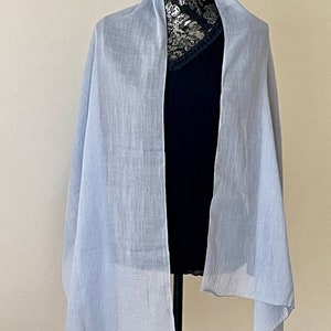 May include: A light blue sheer scarf draped over a mannequin. The scarf is made of a lightweight fabric and has a soft, flowing drape.
