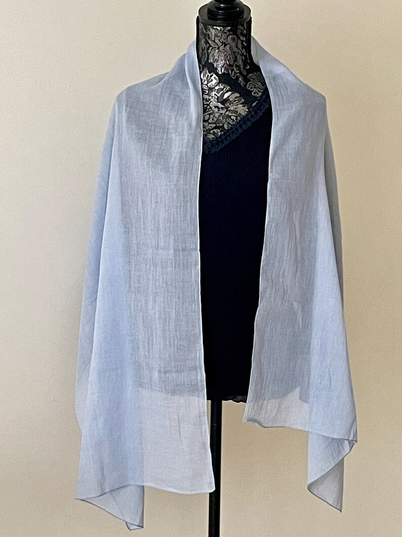 May include: A light blue sheer scarf draped over a mannequin. The scarf is made of a lightweight fabric and has a soft, flowing drape.