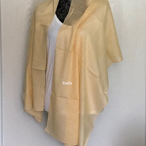 May include: A light yellow sheer scarf draped over a mannequin. The scarf is made of a soft, lightweight fabric and has a subtle sheen. The text "Vanilla" is printed on the scarf.