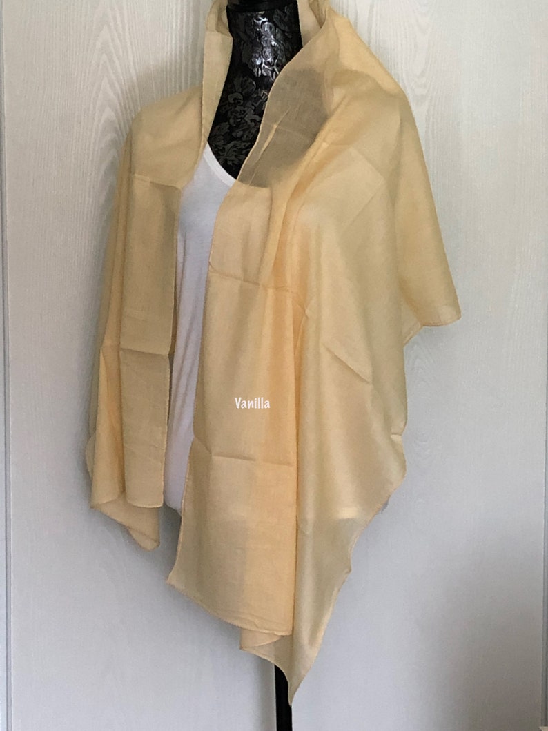 May include: A light yellow sheer scarf draped over a mannequin. The scarf is made of a soft, lightweight fabric and has a subtle sheen. The text "Vanilla" is printed on the scarf.