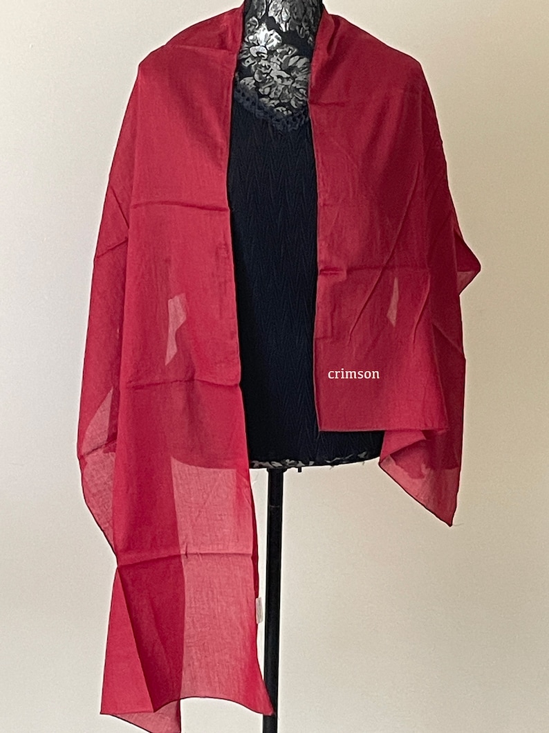 May include: A crimson red sheer scarf draped over a mannequin. The scarf is made of a lightweight fabric and has a flowing drape.