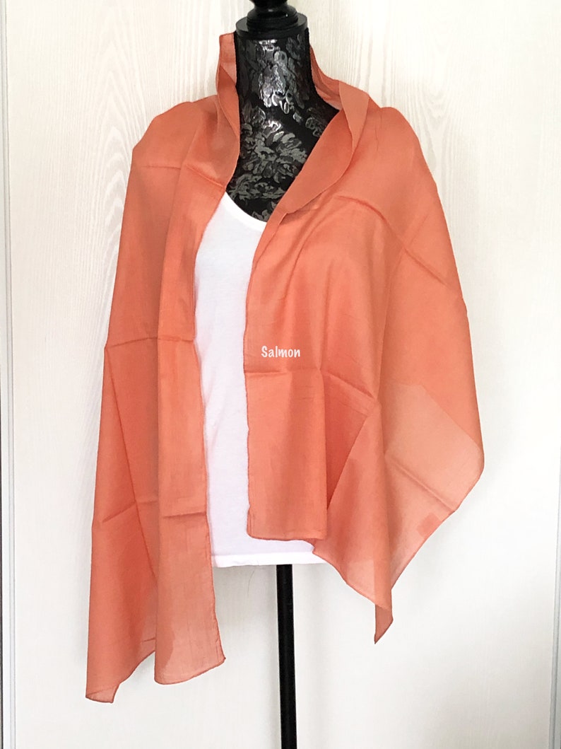May include: A salmon colored sheer scarf draped over a white mannequin. The scarf is made of a lightweight fabric and has a soft, flowing drape.