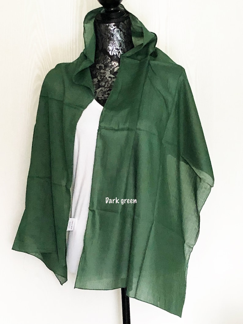 May include: A dark green sheer scarf draped over a white shirt on a mannequin. The scarf is made of a lightweight fabric and has a simple design.