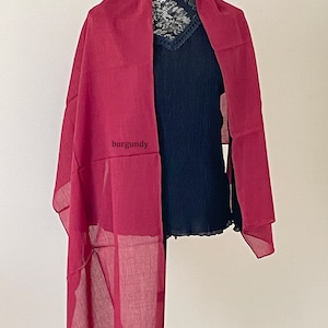 May include: A burgundy sheer scarf draped over a black top on a mannequin.