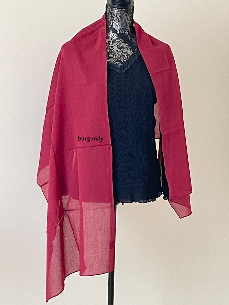May include: A burgundy sheer scarf draped over a black top on a mannequin.