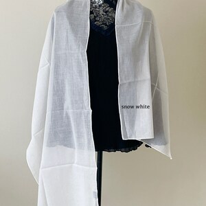 May include: A white sheer scarf draped over a mannequin. The scarf is made of a lightweight fabric and has a soft, flowing drape. The text "snow white" is written on the scarf.