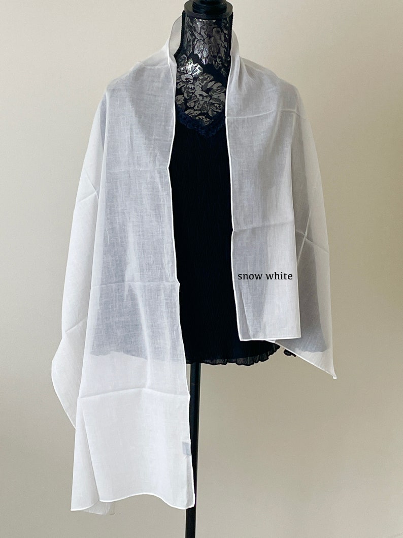 May include: A white sheer scarf draped over a mannequin. The scarf is made of a lightweight fabric and has a soft, flowing drape. The text "snow white" is written on the scarf.
