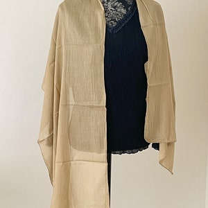May include: A light beige scarf made of a soft, sheer fabric. The scarf is draped over a mannequin and is folded in half.