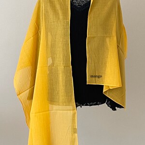 May include: A yellow sheer scarf with the word "mango" printed on it.