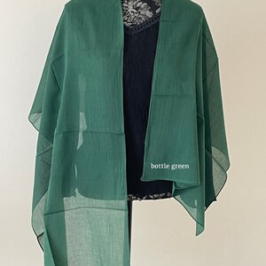 May include: A bottle green sheer scarf draped over a mannequin. The scarf is made of a lightweight fabric and has a simple design.