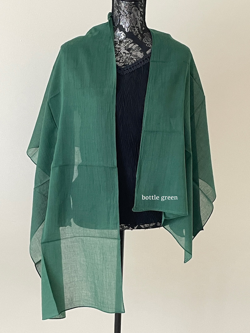 May include: A bottle green sheer scarf draped over a mannequin. The scarf is made of a lightweight fabric and has a simple design.