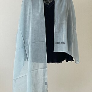 May include: A pale grey sheer scarf draped over a mannequin. The scarf is made of a lightweight fabric and has a soft, flowing drape.