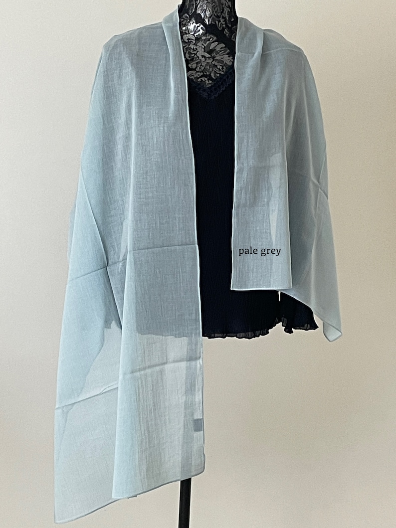 May include: A pale grey sheer scarf draped over a mannequin. The scarf is made of a lightweight fabric and has a soft, flowing drape.