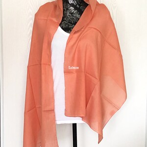 May include: A salmon colored sheer scarf draped over a white mannequin. The scarf is made of a lightweight fabric and has a soft, flowing drape.
