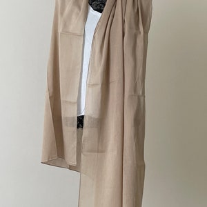 May include: A light brown sheer scarf draped over a mannequin. The scarf is made of a lightweight fabric and has a simple, elegant design.
